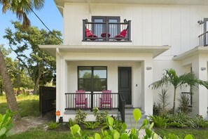 Ein zweistöckiges Haus mit Balkon, Eingangstür und einer kleinen Veranda mit Sitzgelegenheiten.