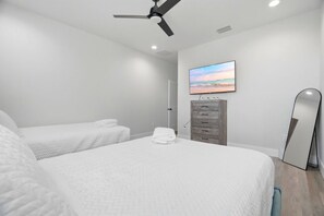 Habitación de hotel con dos camas, ventilador de techo, televisión de pantalla plana, cómoda y un espejo grande.