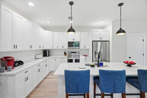 A modern kitchen with white cabinets, stainless steel appliances, and blue chairs around a central island. - Cherry St Chateau | Immaculate Home In Old West Tampa, 5 Min to Ray J (Tampa)