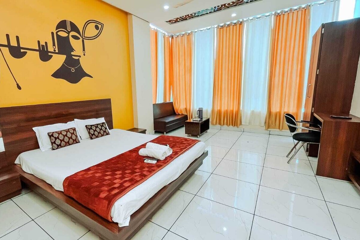 A hotel room with a large bed, a desk, a chair, and a reception area.
