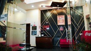 Un espace d’accueil d’hôtel au design moderne, comprenant un comptoir d’accueil, un réfrigérateur Coca-Cola et une cloison en verre.