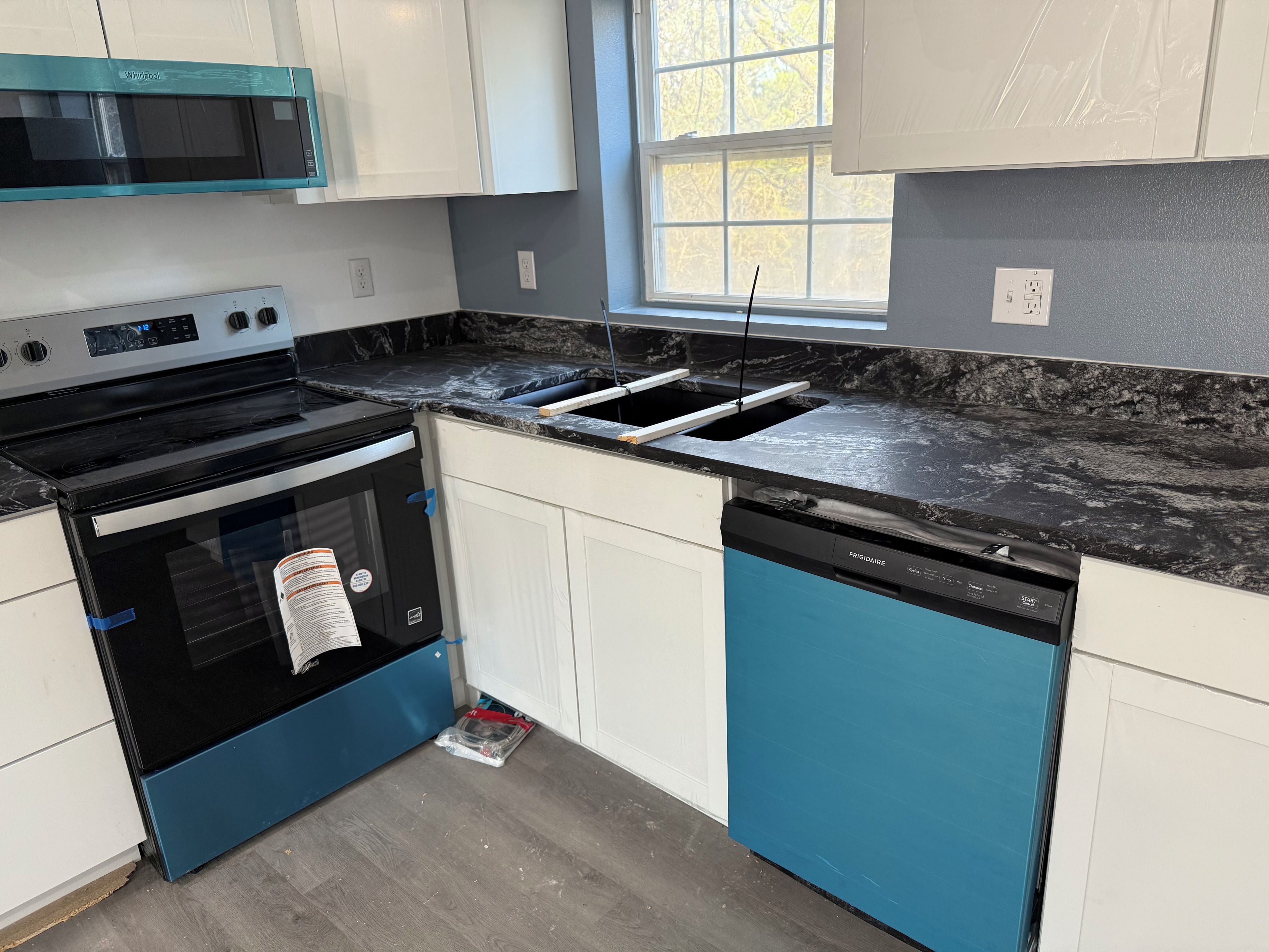 A modern kitchen with a black and blue color scheme, a built-in microwave, a dishwasher, and a window providing natural light.