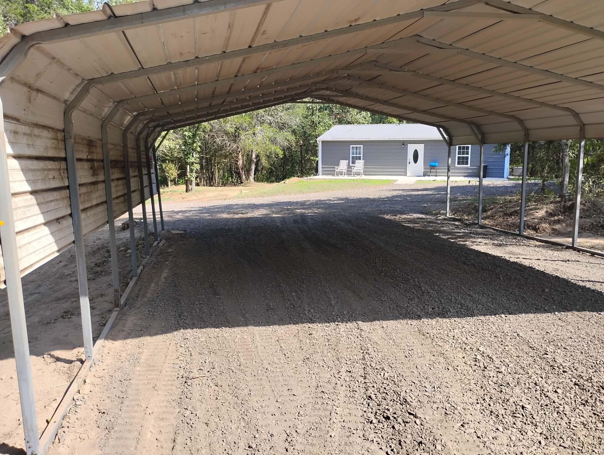 A covered outdoor area with a dirt floor, metal beams, and a building in the background.
