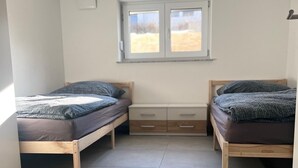 A small, bright room with two wooden beds, a window, and a white wall. - Guesthouse Wain- quiet, comfort, newly renovated.  Pet friendly! (Wain)