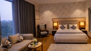 A modern hotel room with a large bed, a sofa, a chair, and a small table. - The Aviyaan (Lucknow)