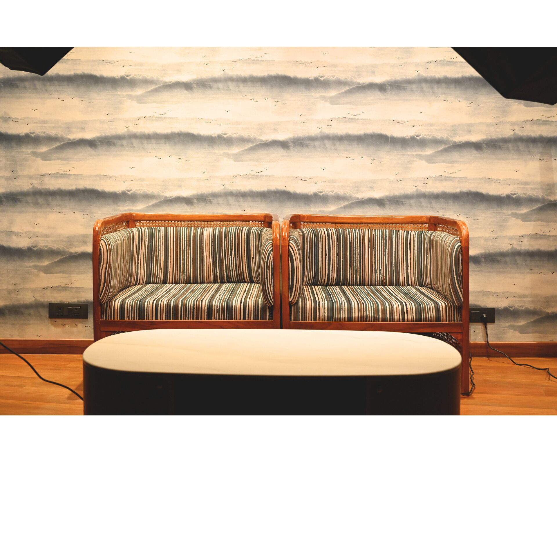 A room with two striped sofas and a round table, against a wall with a wave pattern mural.