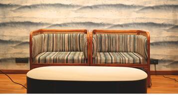 A room with two striped sofas and a round table, against a wall with a wave pattern mural.