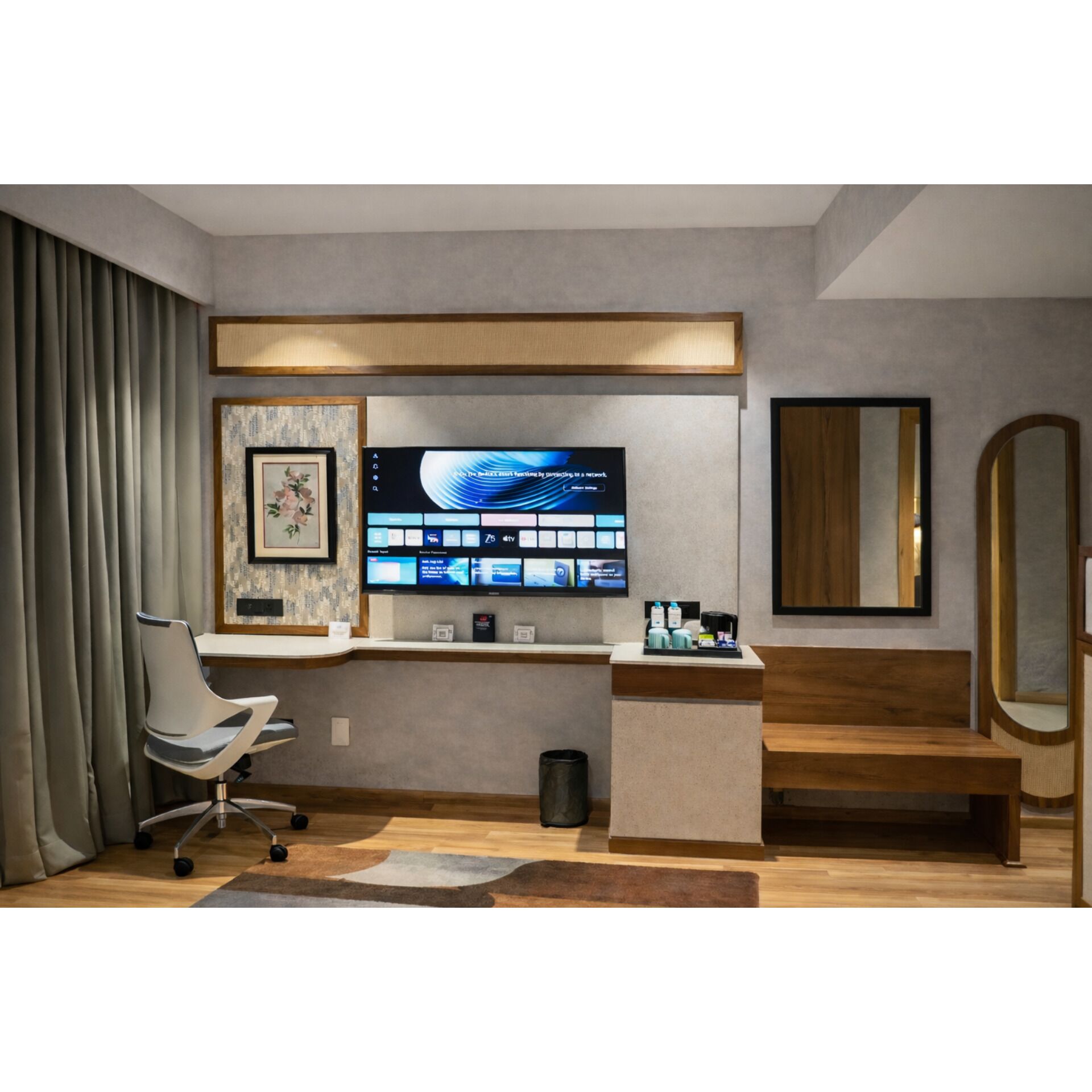 Une chambre d’hôtel moderne équipée d’un bureau, d’une grande télévision à écran plat, d’un tableau encadré, d’un miroir et d’un banc.