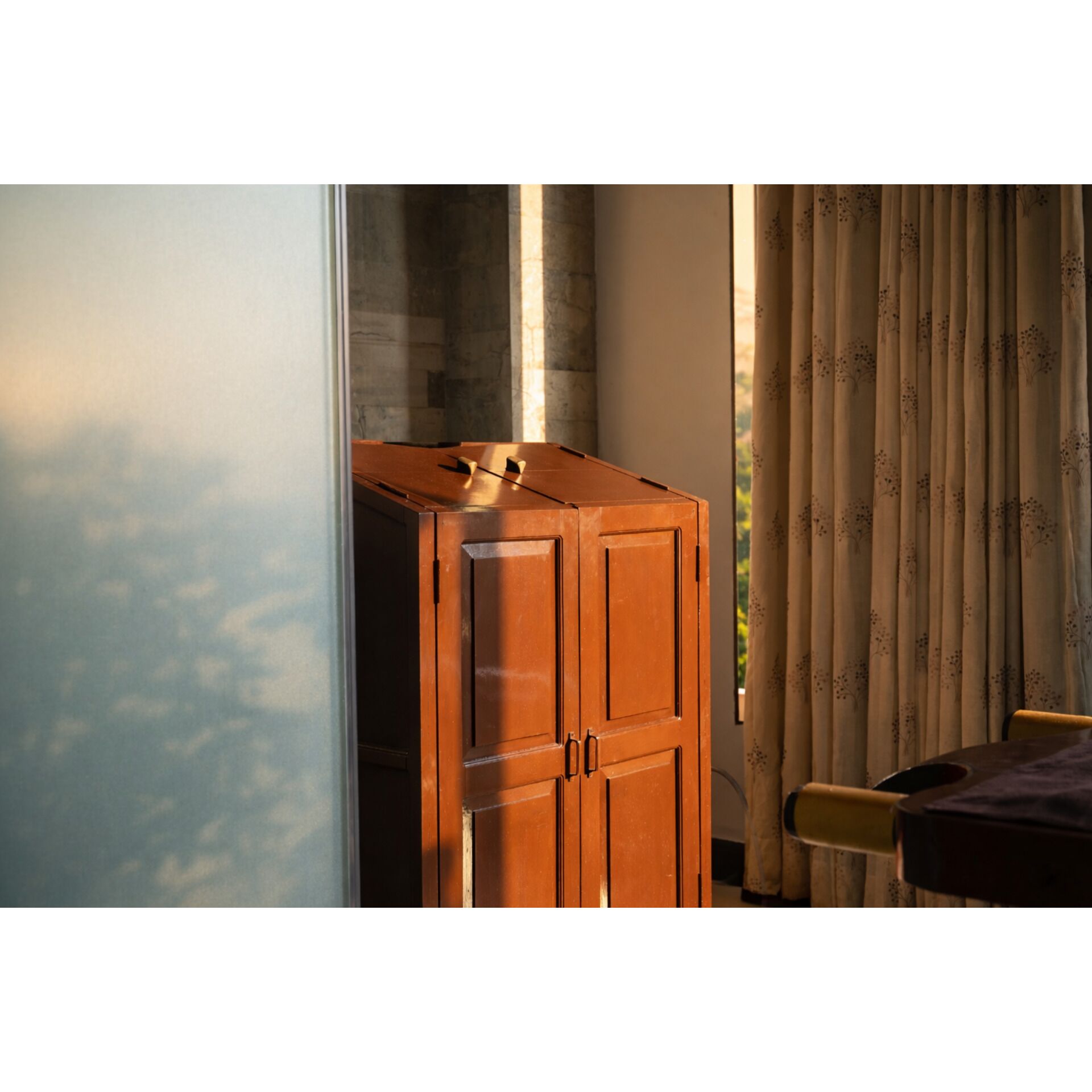 Un mueble de madera con dos puertas, una ventana con cortinas y una mesa con una silla.