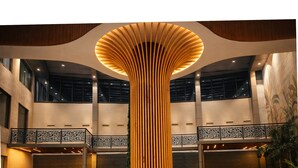 A spacious lobby with a central wooden column, a circular seating area, and a mezzanine level with a railing. - The Aviyaan (Lucknow)