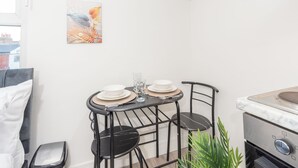 A compact kitchen with a dining table set for two, a modern stove, and a single chair. - Tooting Elite Studios, 5 Mints from Station (London)