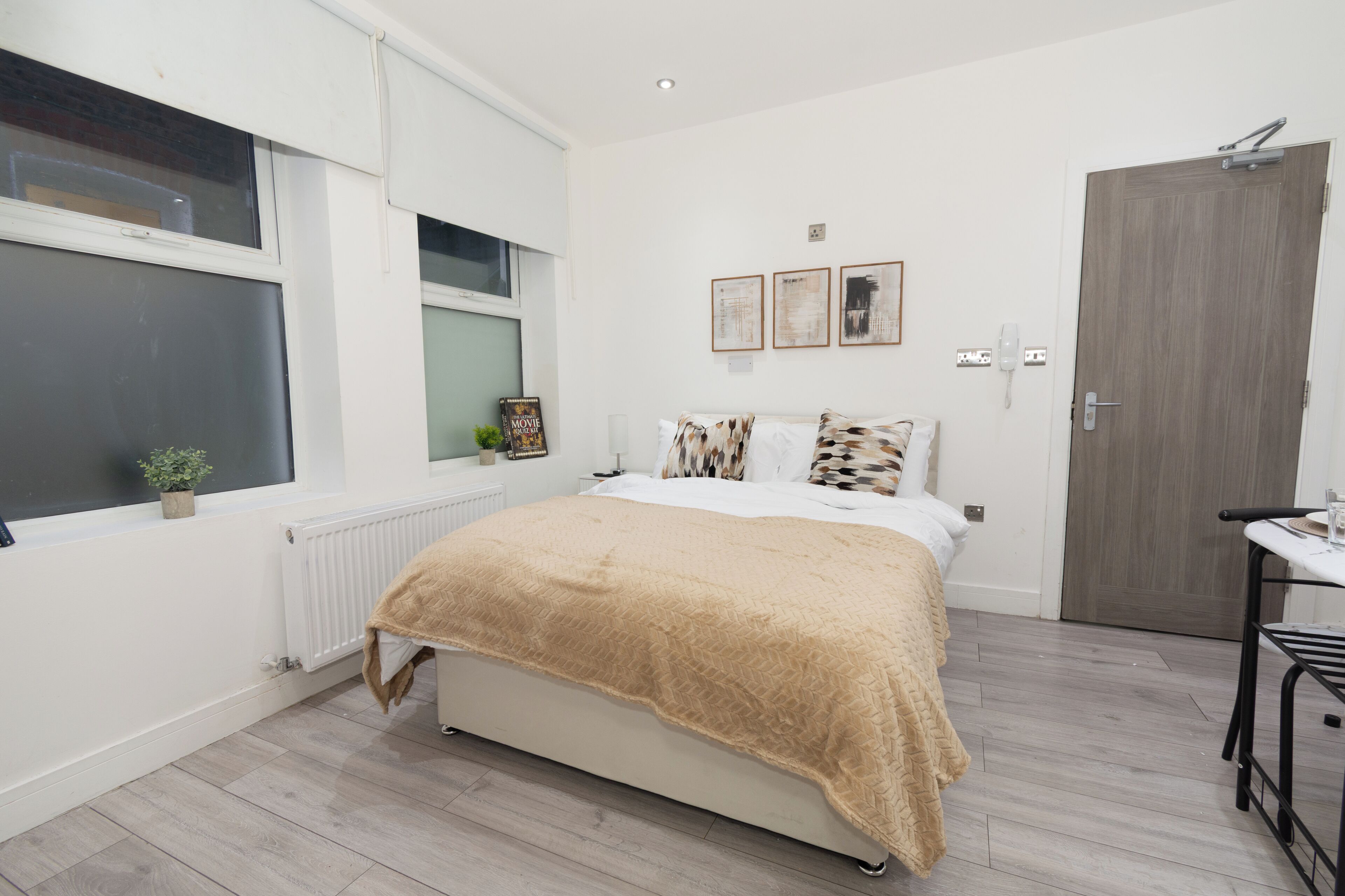 Une chambre à coucher avec un lit, un radiateur, une fenêtre, une porte et une petite table.