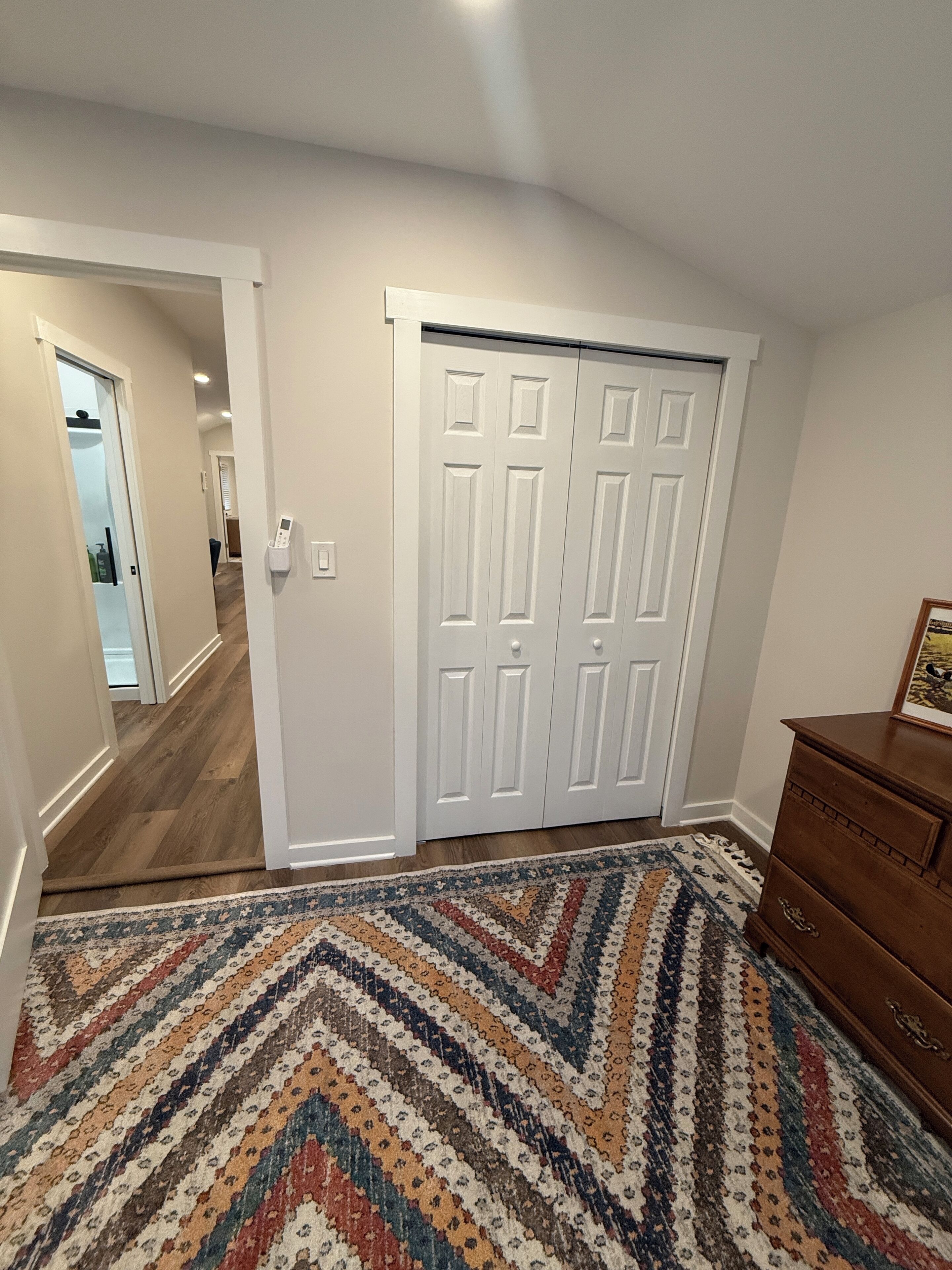 Una habitación con un armario grande de color blanco, un tocador de madera y una alfombra estampada.