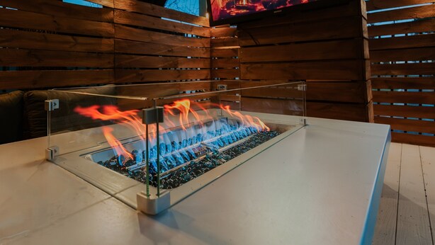 A fire feature with a glass enclosure, wooden panel walls, and a mounted TV screen displaying a fire. - Ultimate World Cup Location|Steps to Westport & KC Streetcar (Kansas City)