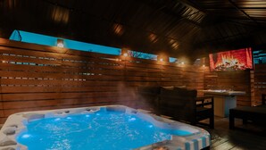 A hot tub in a wooden cabin with a fireplace and a television displaying a fire. - Ultimate World Cup Location|Steps to Westport & KC Streetcar (Kansas City)