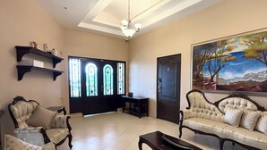 Amplia sala de estar con techo alto, un candelabro, un conjunto de sofás, una mesa de centro y un cuadro en la pared.