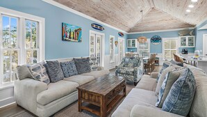 A living room with a wooden ceiling, a large window, and a dining area with a table and chairs. - 6 Bikes! Ride Golf Cart to Beach & Pool! ~ The Star of the Sea in Magnolia Cottages on 30A (Seacrest)