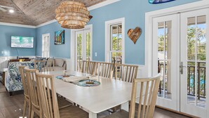 A dining area with a white table and wooden chairs, a woven ceiling light, and a view of the outdoors through large windows. - 6 Bikes! Ride Golf Cart to Beach & Pool! ~ The Star of the Sea in Magnolia Cottages on 30A (Seacrest)