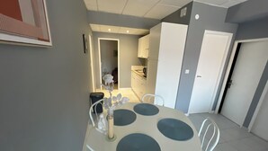 Een eetruimte met een ronde tafel en stoelen, een keuken op de achtergrond en een deur aan de rechterkant.