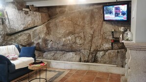 A living room with a stone wall, a blue sofa, a television mounted on the wall, and a tiled floor. - Private Pool With Huge Terrace Garden (Celorico de Basto)