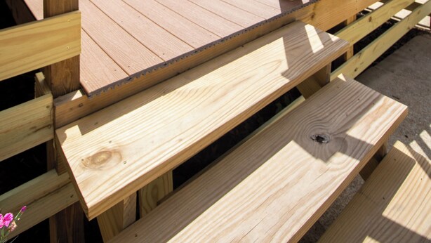 Een houten terras met banken, een hekwerk en uitzicht op bomen en de lucht.