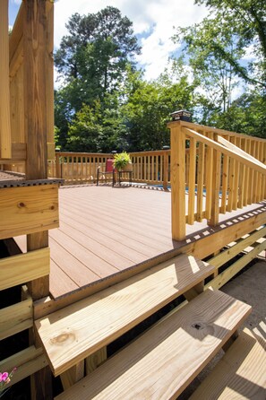 A wooden deck with benches, a railing, and a view of trees and sky.