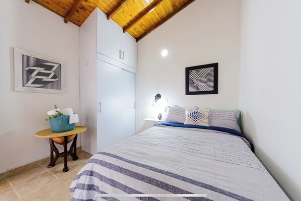 Un dormitorio con una cama, una mesita de noche con una cesta y un armario.