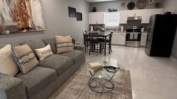 Una sala moderna con un sofá gris, una mesa de centro de vidrio y una alfombra.
