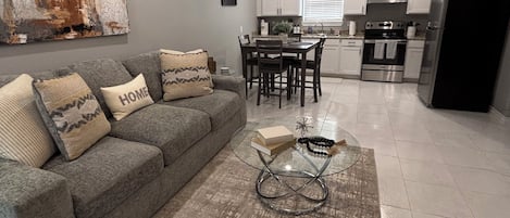 A modern living room with a gray sofa, a glass coffee table, and a rug.