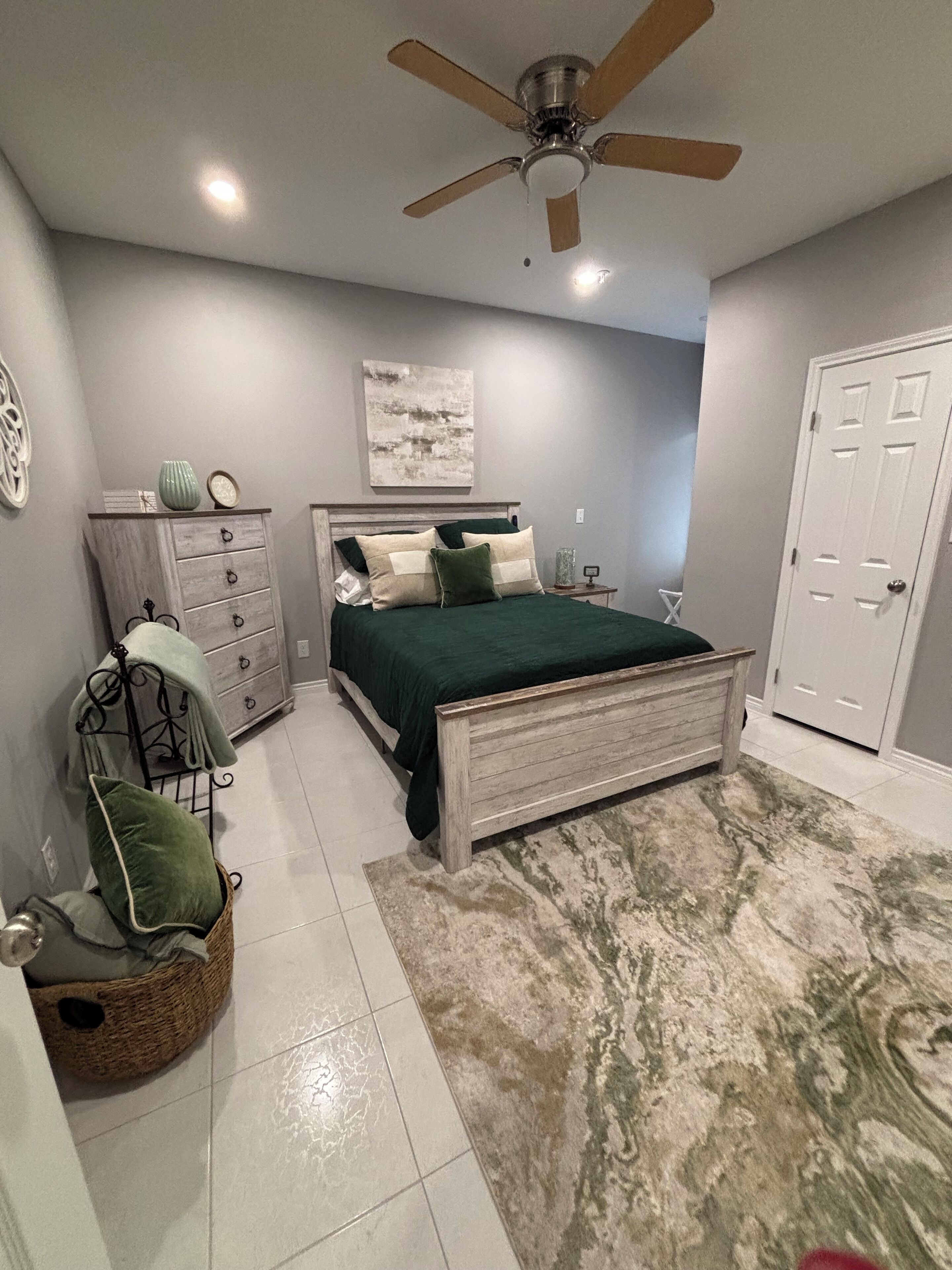 Un dormitorio con cama, cómoda, silla y ventilador de techo.