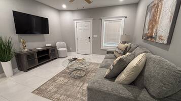 A modern living room with a grey sofa, a coffee table, a TV, and a ceiling fan.