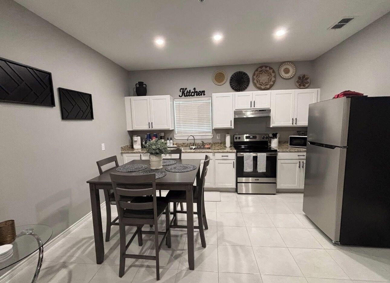 Una cocina moderna con armarios blancos, un refrigerador de acero inoxidable y un comedor con mesa y sillas.