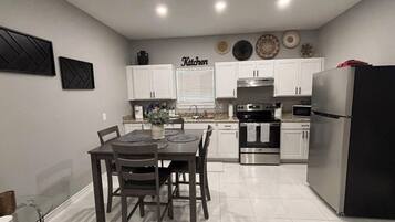 Una cocina moderna con armarios blancos, un refrigerador de acero inoxidable y un comedor con mesa y sillas.