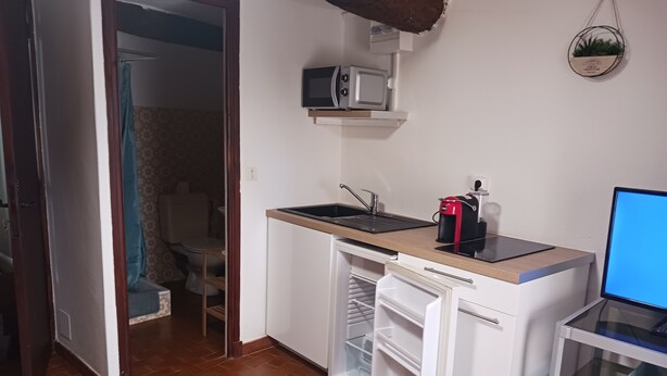 Pieni, käytännöllinen keittiö, jossa on mikroaaltouuni, kahvinkeitin ja pöydällä tietokone.