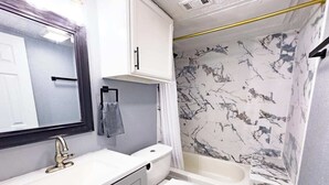 Une salle de bain avec un lavabo blanc, un miroir et des toilettes, un porte-serviettes et une baignoire dont les murs sont décorés d’un motif imitant le marbre.