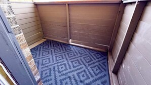 Un petit espace extérieur clos, avec un tapis bleu à motifs sur le sol, des murs en bois et une fenêtre en haut.