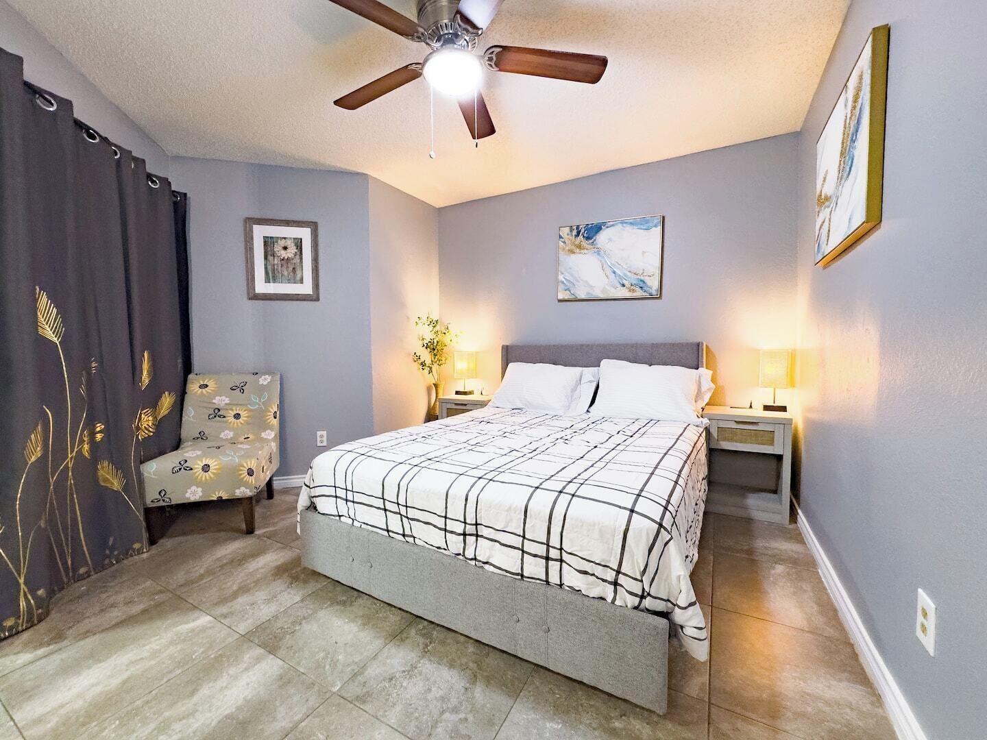 A bedroom with a bed, a ceiling fan, a nightstand, a chair, and two wall-mounted lamps.
