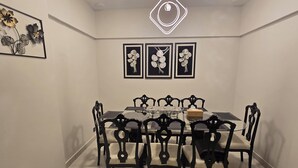 A dining area with a round table, black chairs, and framed floral artwork on the wall. - Karachi Beach Residency (Karachi)