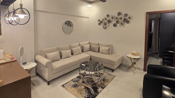 A modern living room with a beige sectional sofa, a round coffee table, a ceiling fan, and decorative wall art. - Karachi Beach Residency (Karachi)