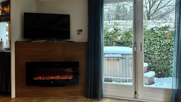 Un soggiorno con televisione a schermo piatto sopra un caminetto e una porta vetrata scorrevole che dà su un giardino innevato.