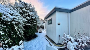 Un sentiero innevato conduce a un edificio con il cartello 'Relax 10', circondato da alberi e arbusti carichi di neve.