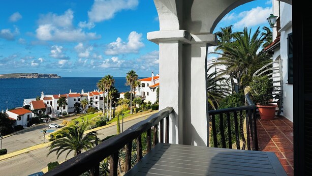 A balcony with a view of a coastal town, palm trees, and a clear blue sky. - Island Paradise, peace and quiet with stunning views across to the lighthouse. (Platges de Fornells)