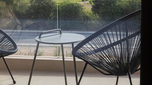 Un balcón con dos sillas y una mesa, con vistas a un paisaje costero con vegetación y al mar.