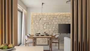 Una sala de estar moderna con una pared de piedra, un área de comedor con una mesa lista para dos personas y un sofá.