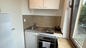 A compact kitchen with white cabinets, a built-in oven, and a window providing a view of the street. - Studio 2 beds Kitchen BAD TV Wlan (Bremen)