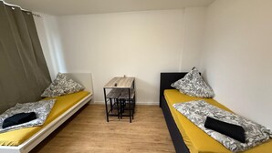 A small, compact room with two single beds, a small table, and a bench. - Studio 2 beds Kitchen BAD TV Wlan (Bremen)