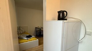 A compact room with a bed, a small table, and a refrigerator. - Studio 2 beds Kitchen BAD TV Wlan (Bremen)