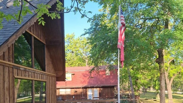 Une terrasse en bois avec des meubles d’extérieur, un mât portant le drapeau américain et, au fond, un bâtiment rouge.