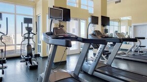 Un gimnasio con cintas de correr, equipo de ejercicio y amplias ventanas que dejan entrar luz natural.