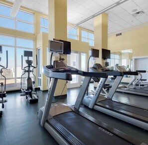 Ein Fitnessstudio mit Laufbändern, Trainingsgeräten und großen Fenstern für natürliches Licht.
